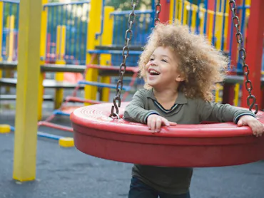 Child playing and thriving using tire swing set in the playground.