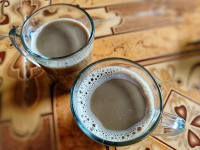 Freshly brewed warm milk coffee is served in a clear glass with a blur background