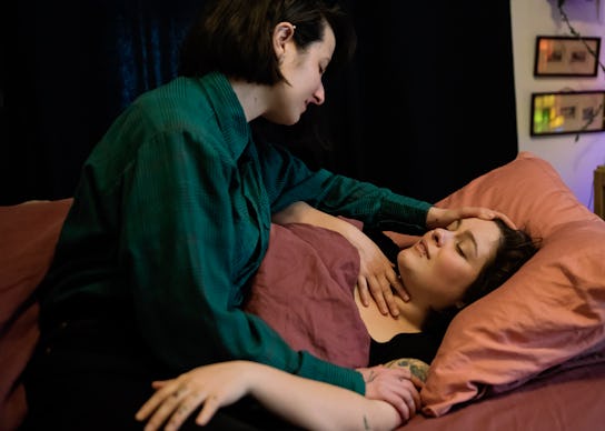 Young woman comforting partner who is lying in bed with a sore throat. Both women are in their late ...