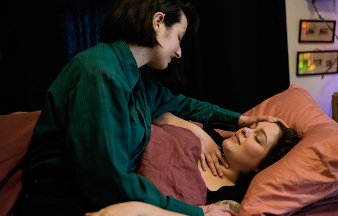 Young woman comforting partner who is lying in bed with a sore throat. Both women are in their late ...