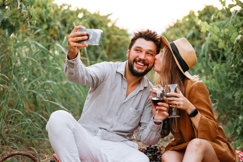 Young cheerful couple drinking wine and toasting with wineglasses in vineyard