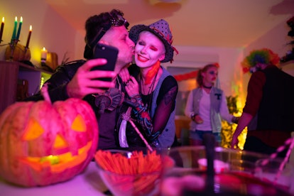 Young couple taking Instagram selfies at the Halloween party.