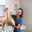 A mid adult woman getting a mammogram. She is being helped by an African-American nurse.