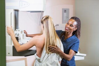 A mid adult woman getting a mammogram. She is being helped by an African-American nurse.