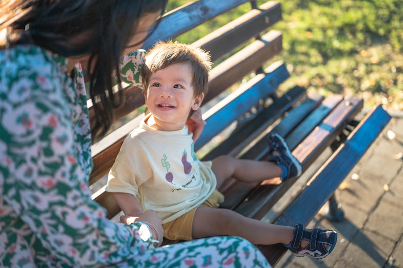 Woman and her one year old baby boy sitting on the park bench at sunset spending time outdoors.