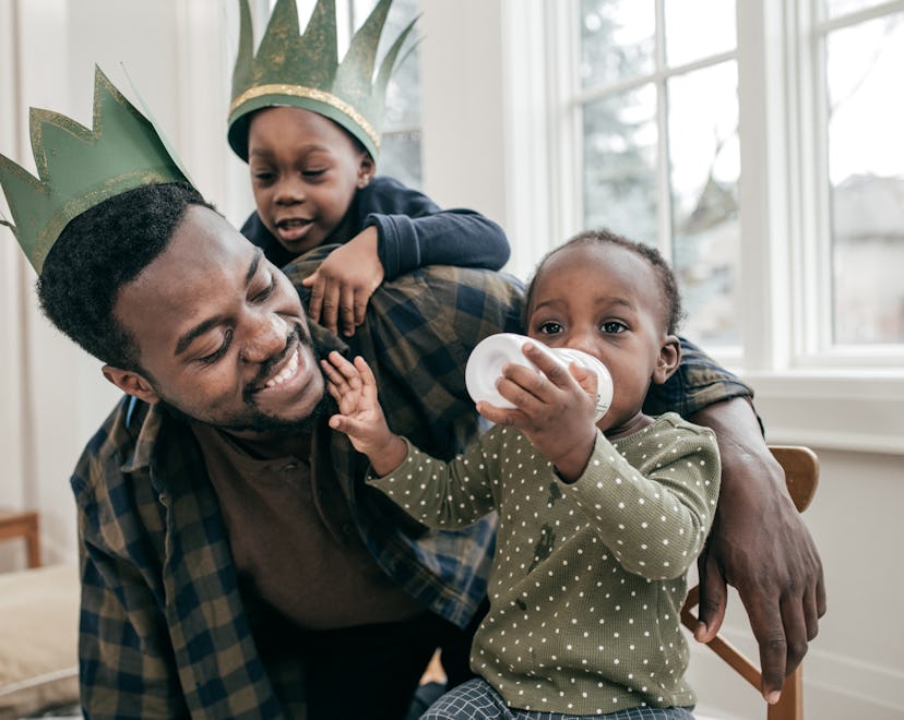 Dad plays with two sons, while he and the younger boy wear crowns in an article of baby names like L...