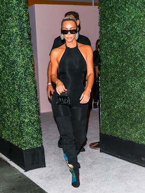Kim Kardashian in a black body-tight, sleeveless dress, black sunglasses and shiny silver circle ear...