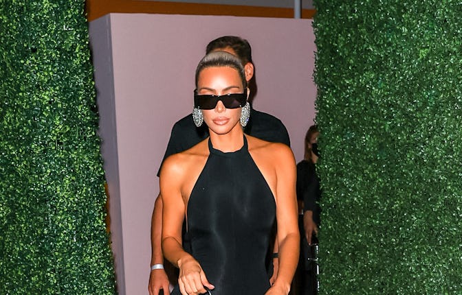 Kim Kardashian in a black body-tight, sleeveless dress, black sunglasses and shiny silver circle ear...