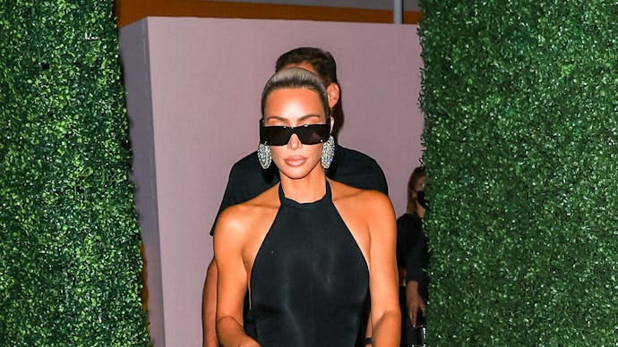 Kim Kardashian in a black body-tight, sleeveless dress, black sunglasses and shiny silver circle ear...