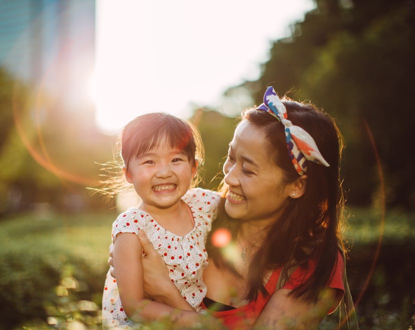 Pretty young mom carrying the lovely toddler girl talking and smiling joyfully with her in the park