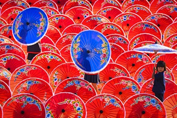 A young girl holding the blue traditional umbrella in a row of red umbrellas outdoors...