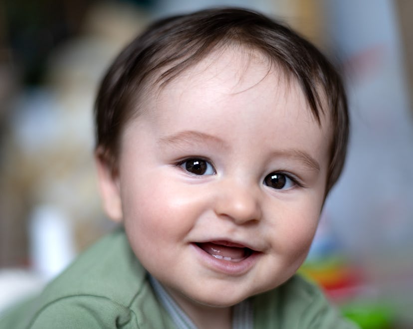 Close up portrait of adorable baby lying on floor looking at camera with his mouth open and smiling.