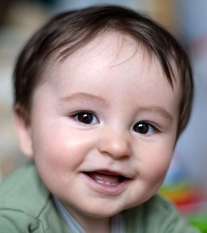 Close up portrait of adorable baby lying on floor looking at camera with his mouth open and smiling.