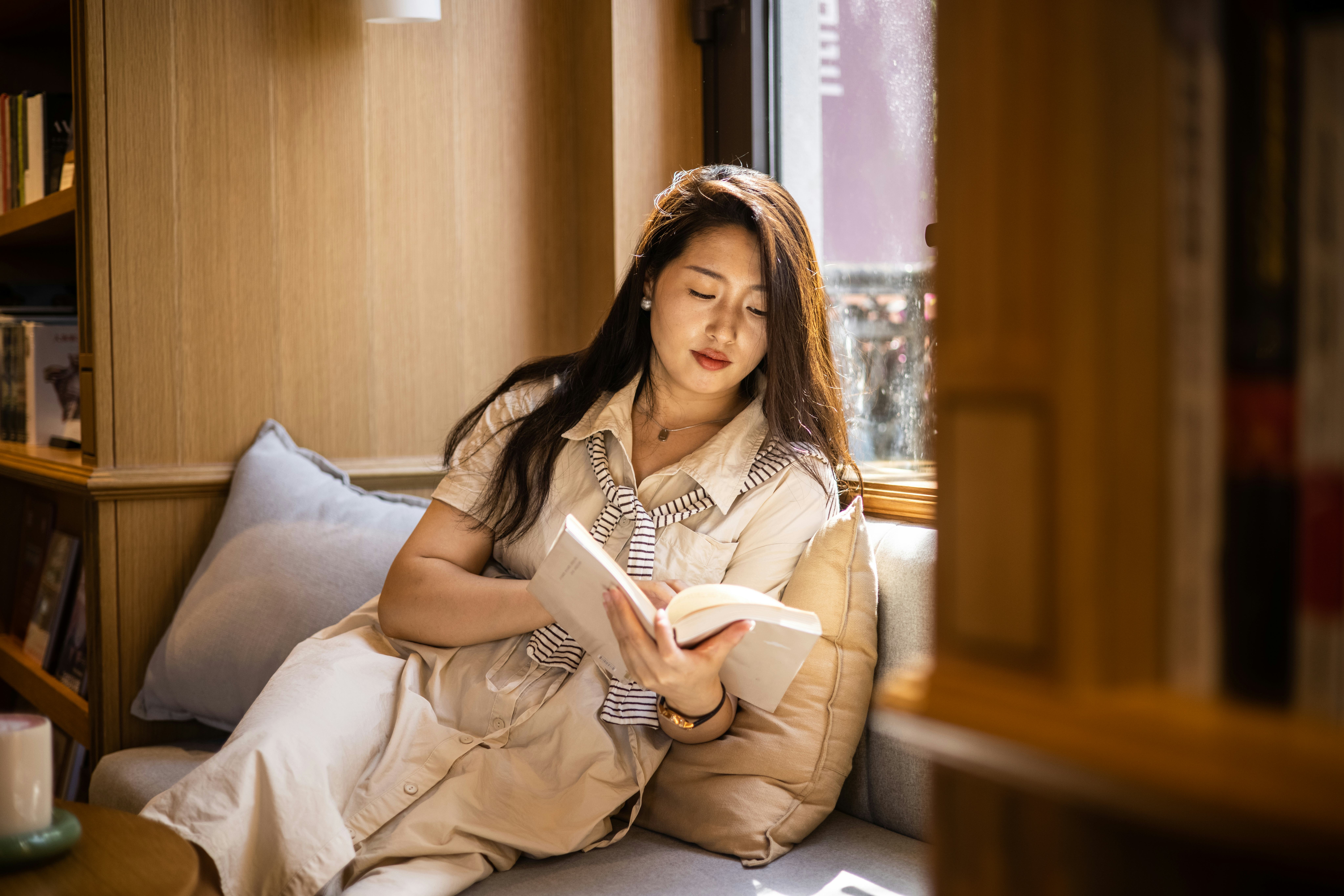 Women reading book sitting on windowsill