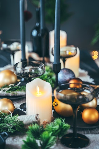 Dark holiday table set up with candle lights, fir tree branches and Christmas balls. Black tableware...