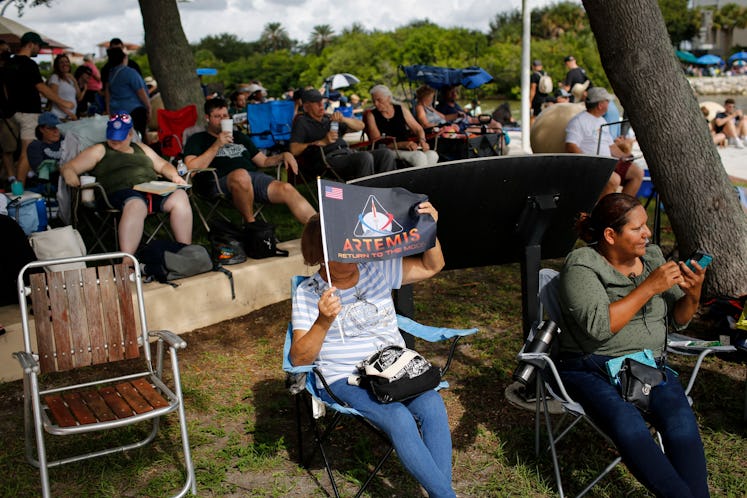 A woman uses an Artemis flag as cover from the sun as she waits for the launch of the Artemis I unma...