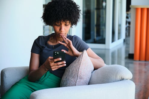 Young businesswoman reading a text message on her phone while sitting in a chair in an office lounge