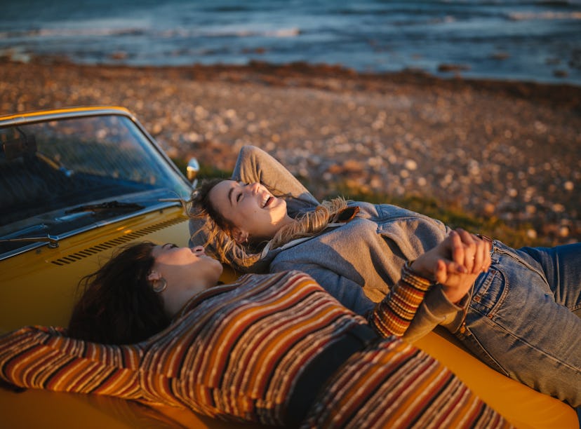 Young hipster girls with vintage convertible car relaxing at the beach at sunset