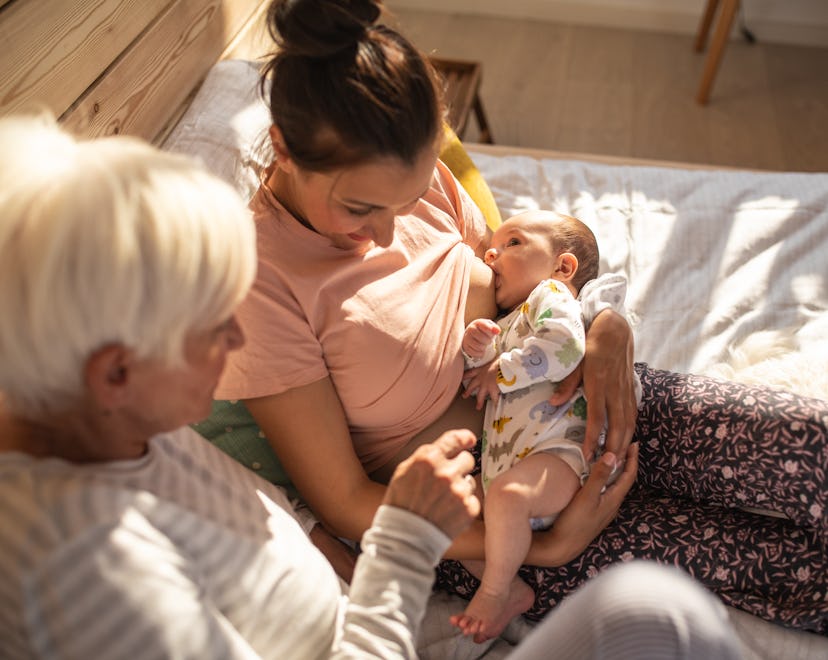 High angle view of Mother breastfeeding baby boy, talking with senior woman, together sitting on be...