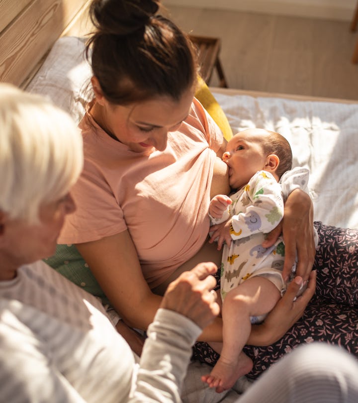 High angle view of Mother breastfeeding baby boy,  talking with senior woman, together sitting on be...