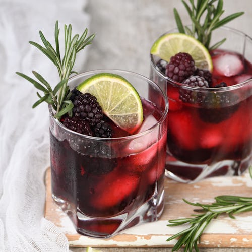 Two glasses of delicious refreshing lemonade with blackberry, ice and lime, decorated of rosemary. C...