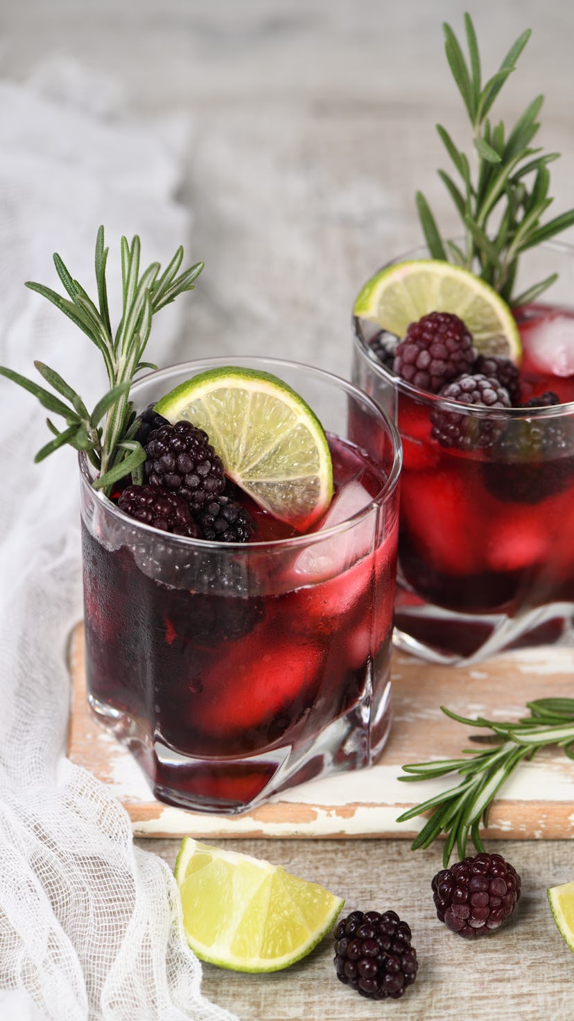 Two glasses of delicious refreshing lemonade with blackberry, ice and lime, decorated of rosemary. C...