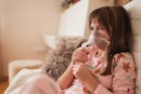 女孩坐在家里的沙发上，用喷雾器和吸入器治疗哮喘。
