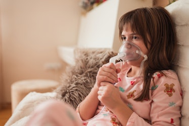 Girl using nebulizer and inhaler for asthma treatment, sitting on the couch at home.