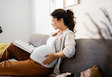 Pregnant woman at home reading a book, probably dealing with pregnancy farts.