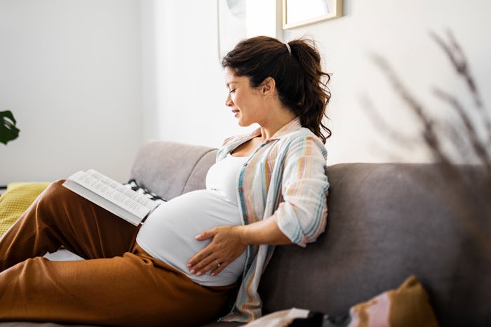 Pregnant woman at home reading a book, probably dealing with pregnancy farts.