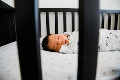 newborn swaddled baby sleeping in modern black crib in article discussing when baby can sleep on sto...