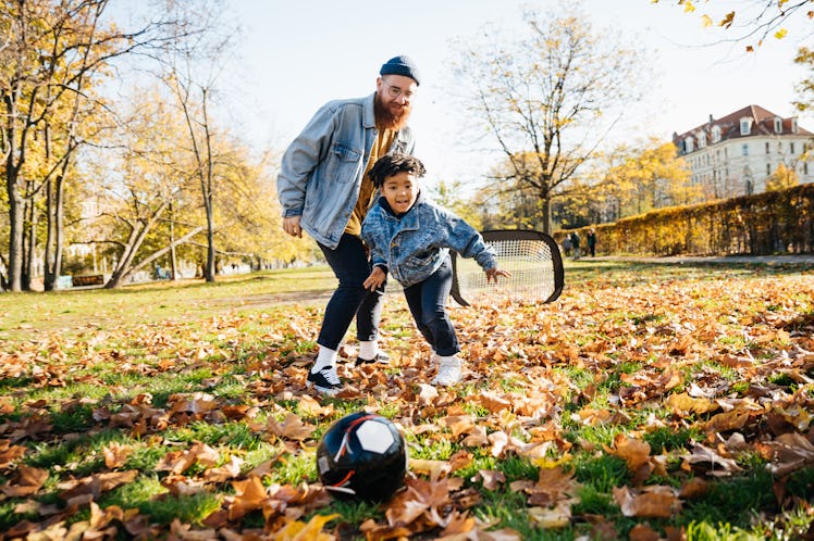 A dad playing soccer with his son while spending the day at the park together.