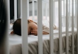 Baby sleeping in cot peacefully with finger in mouth in article discussing when its safe for baby to...