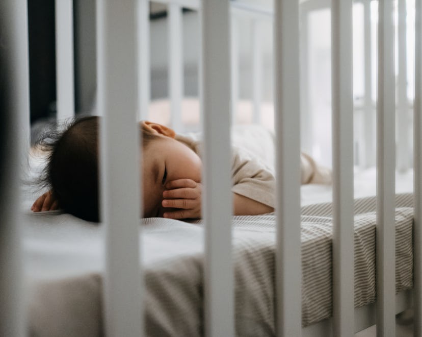 Baby sleeping in cot peacefully with finger in mouth in article discussing when its safe for baby to...