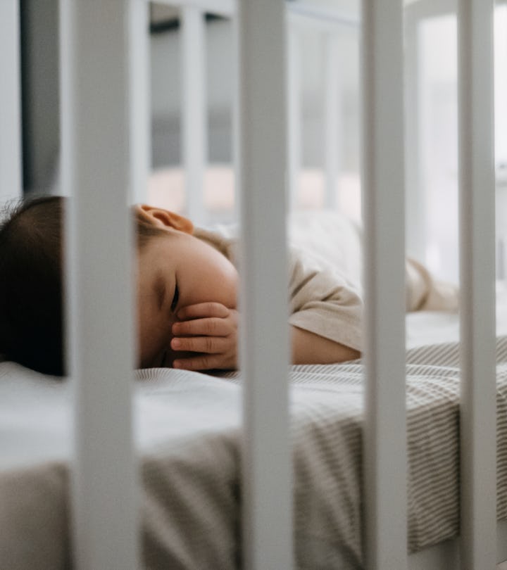 Baby sleeping in cot peacefully with finger in mouth in article discussing when its safe for baby to...