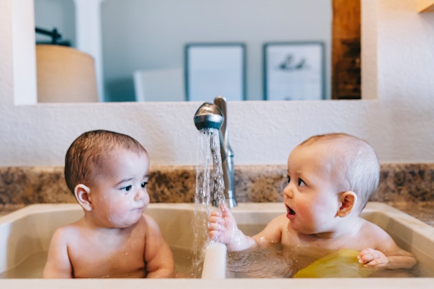 Fraternal twin boys cheerfully play with each other while taking a bath in the sink in article about...