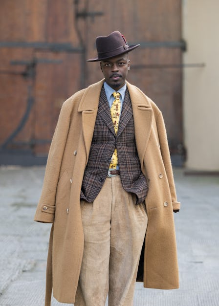 FLORENCE, ITALY - JANUARY 11: A guest wears beige double breasted coat, brown hat, checkered blazer,...