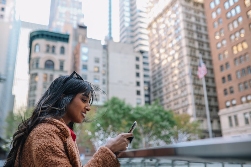 Businesswoman walking in New York, Lower Manhattan, Financial District, using her phone, checking em...