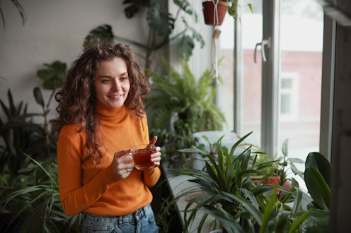 Home greenhouse. Green office and recreation area.Young woman in mustard-colored turtleneck relaxes ...