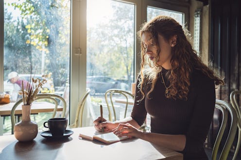 Young Caucasian woman, deep in her thoughts, journaling at the coffee shop