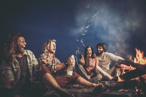 Cheerful friends having fun by the campfire during the autumn night.