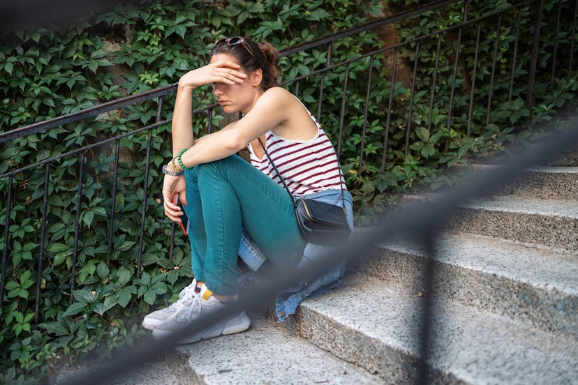 Sad woman sitting on stairs and holding her smartphone