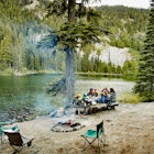 Family and friends sharing a meal together at campsite by lake in mountains
