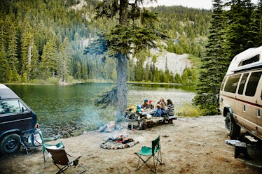 Family and friends sharing a meal together at campsite by lake in mountains