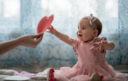 Baby girl reaching for a paper heart, in a story about how to celebrate baby's first Valentine's Day