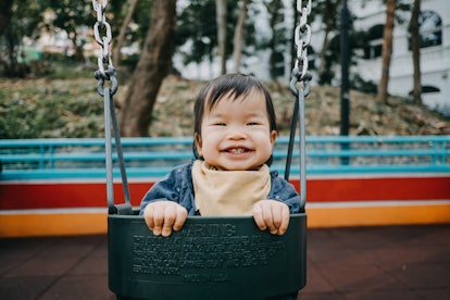 Happy baby girl smiling joyfully playing on swing in playground