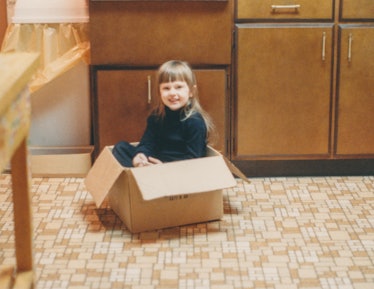 Happy child smiling and sitting in a cardboard box on the kitchen floor, vintage linoleum flooring. ...