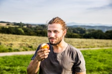 A man outdoors eating an apple.