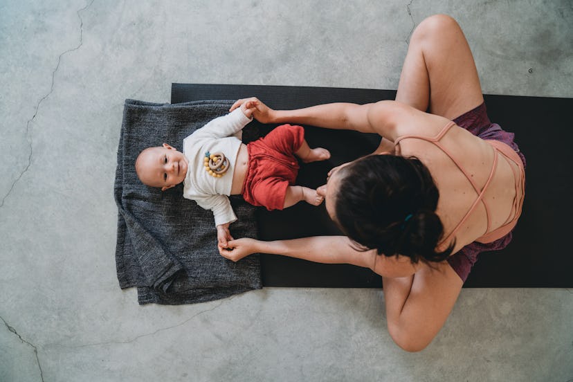 Mother playing with baby on a yoga mat, preparing to do exercises for postpartum back pain.