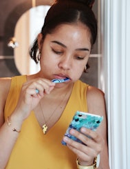 Mixed race young woman, brushing teeth and checking phone outside bathroom